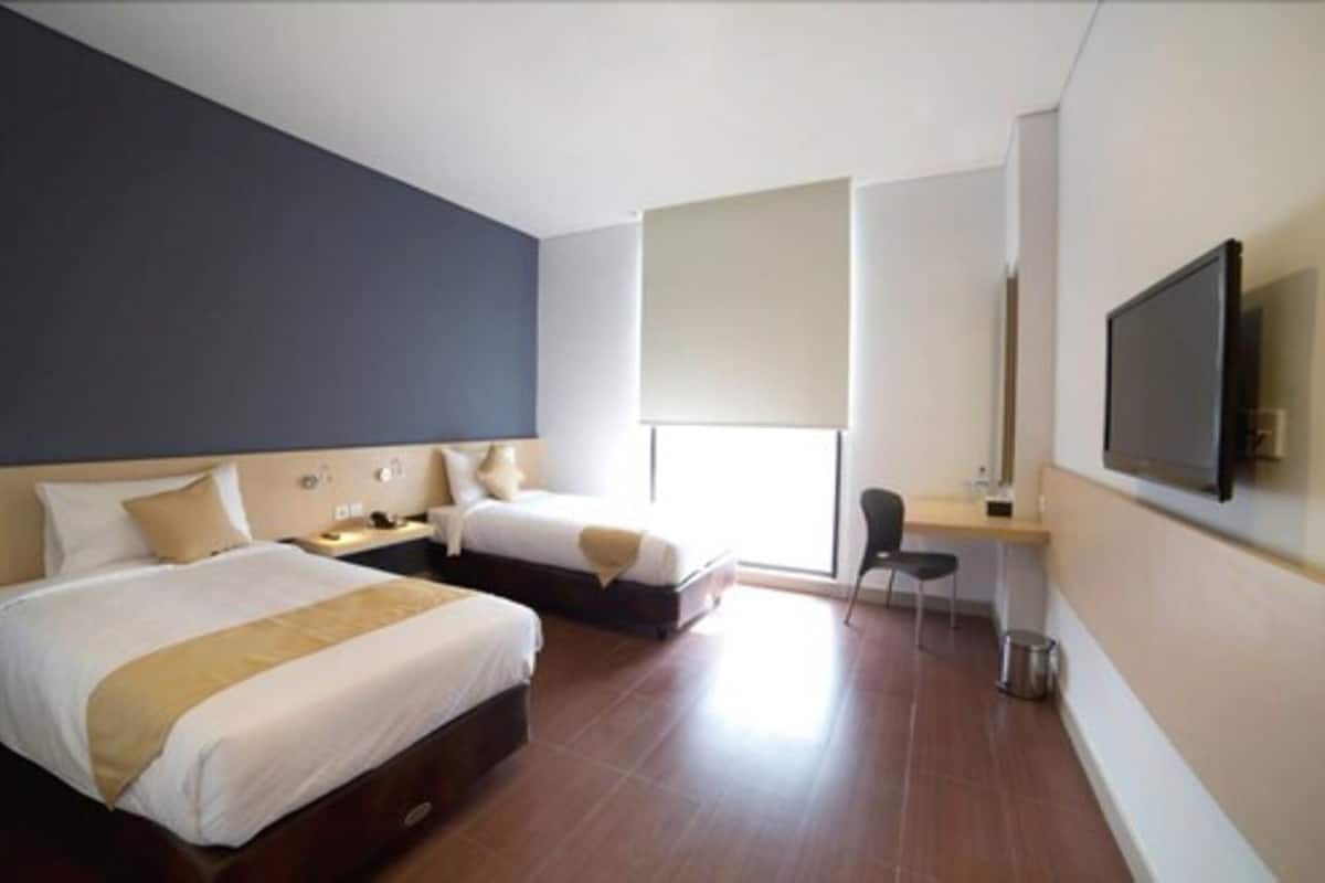 A hotel room with two beds, a desk, a chair, a TV, and a window.