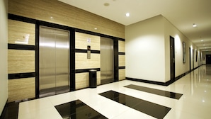 A modern hallway with a polished floor, a wall-mounted elevator, and a trash bin. - Hotel 88 Mangga Besar VIII by WH (Jakarta)