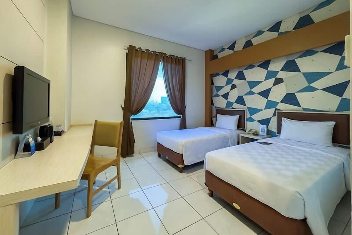 A hotel room with two beds, a desk with a television, a chair, and a window with curtains.