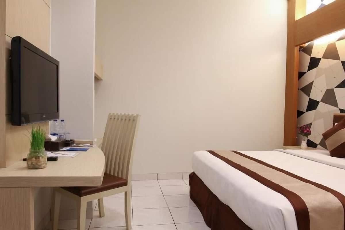 A hotel room with a bed, a desk with a chair, a TV, and a wall with a geometric pattern.