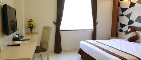 A hotel room with a bed, a desk, a chair, a TV, and a window with curtains.