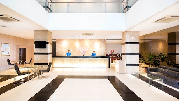 A modern hotel lobby with a reception desk, two receptionists, a seating area with chairs, a sofa, and a large mirror. - Hotel 88 Mangga Besar VIII by WH (Jakarta)
