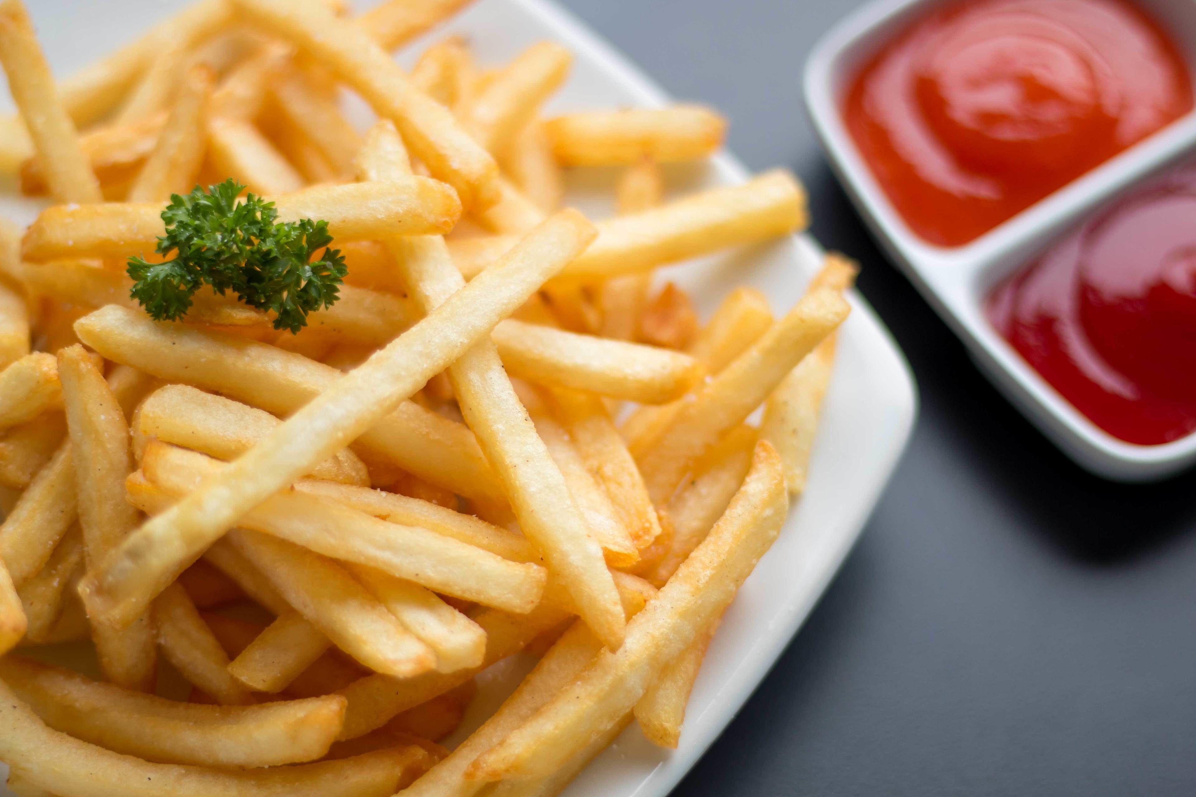 A plate of French fries with a garnish and two small containers of ketchup.