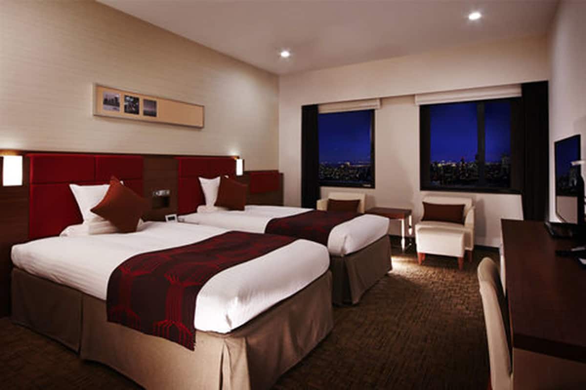 Quarto de hotel com duas camas, uma escrivaninha, uma cadeira e uma televisão.