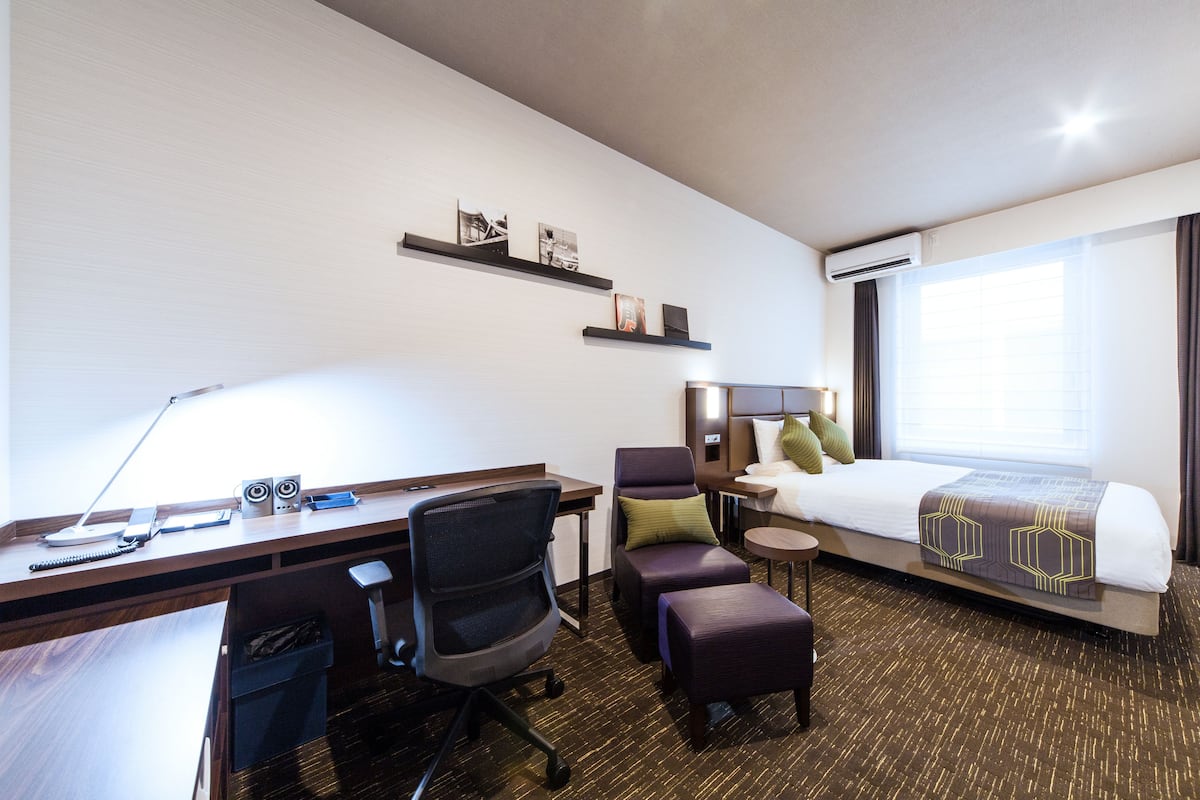 Quarto de hotel com escrivaninha, cadeira, cama e uma pequena mesa.