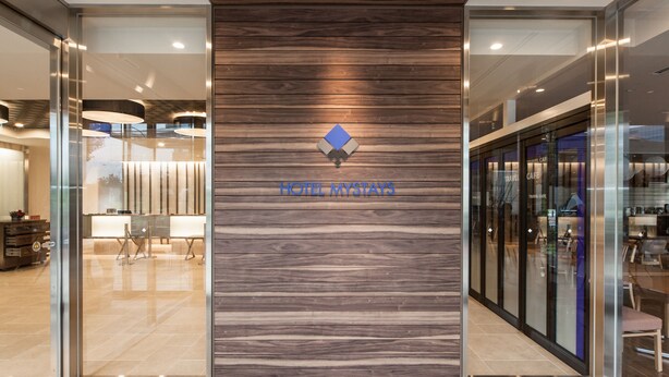 Une entrée d’hôtel moderne avec un mur en bois, des portes en verre et un logo.