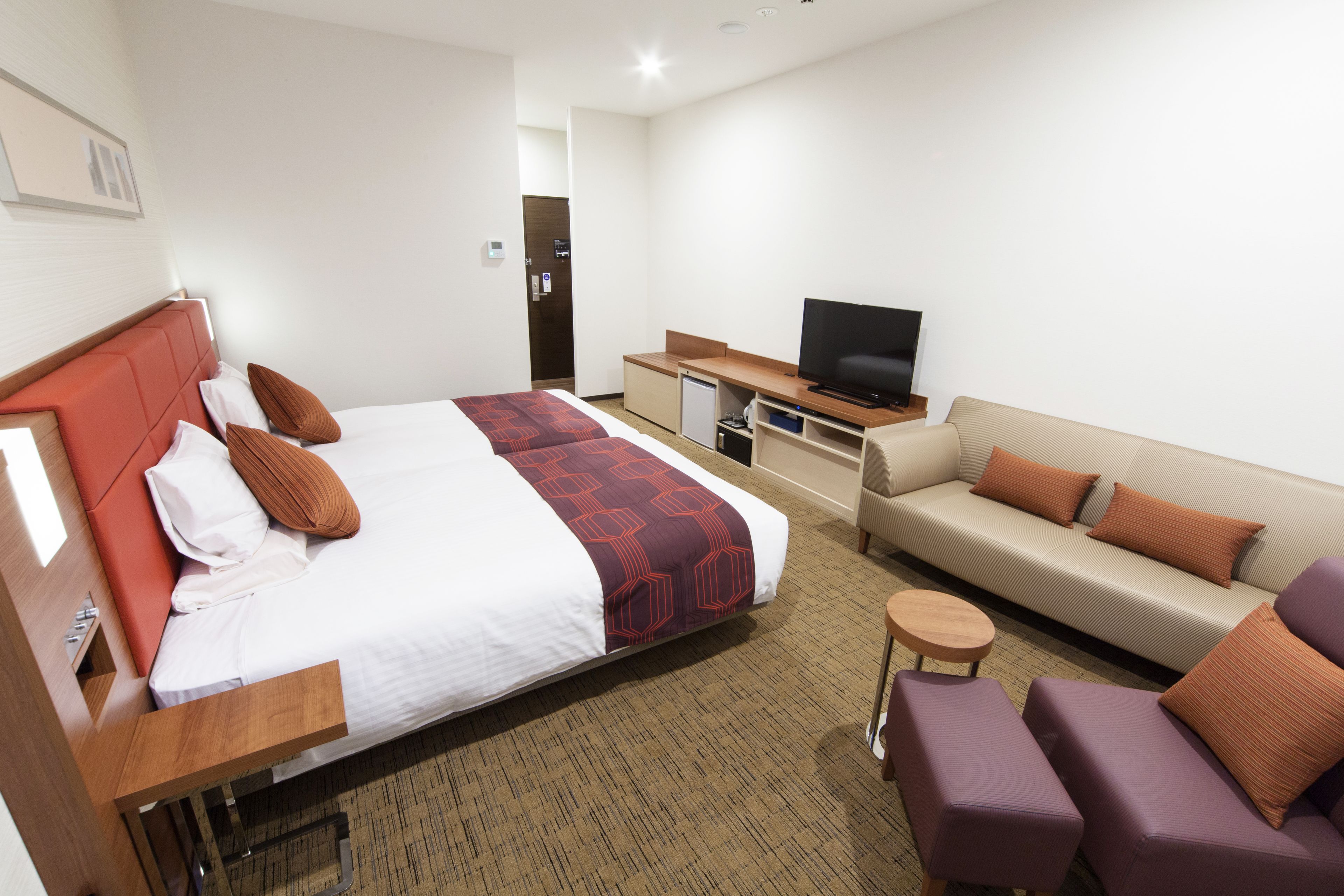 A hotel room with a bed, a sofa, a TV, and a small table.
