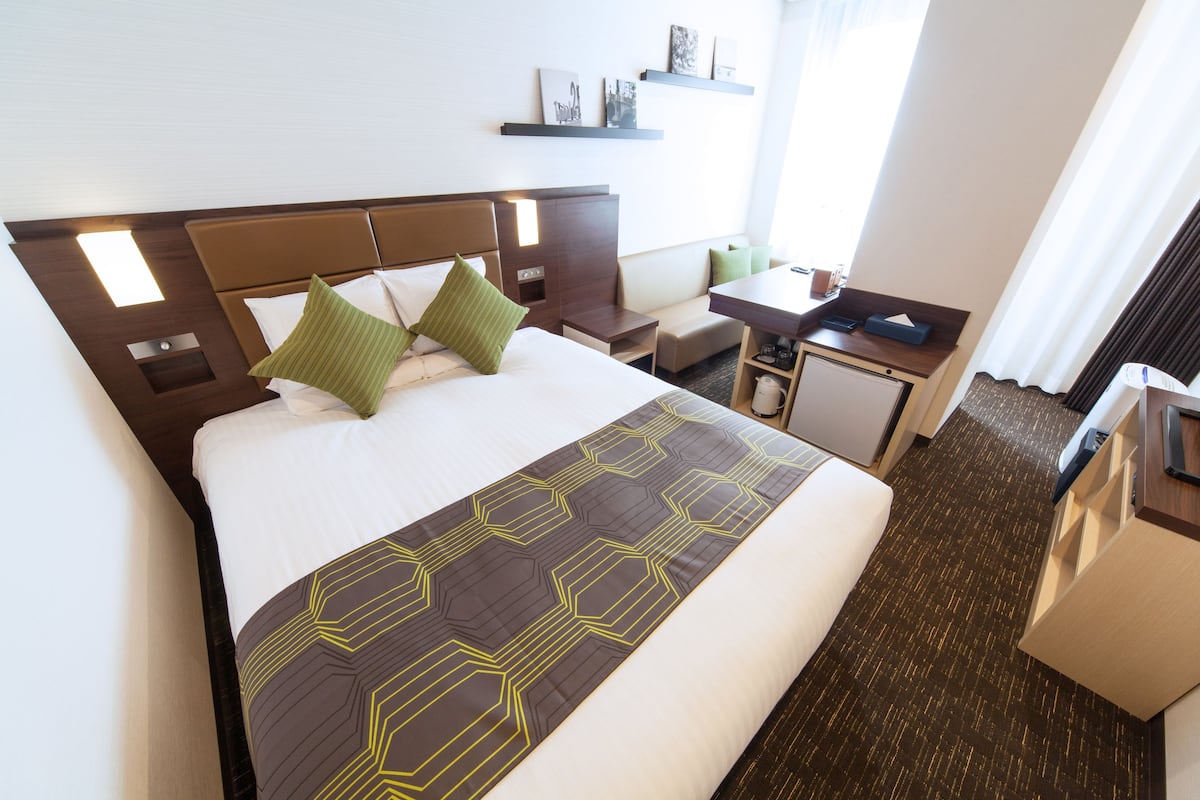 Quarto de hotel com uma cama grande, uma escrivaninha, uma cadeira e uma mesa pequena.