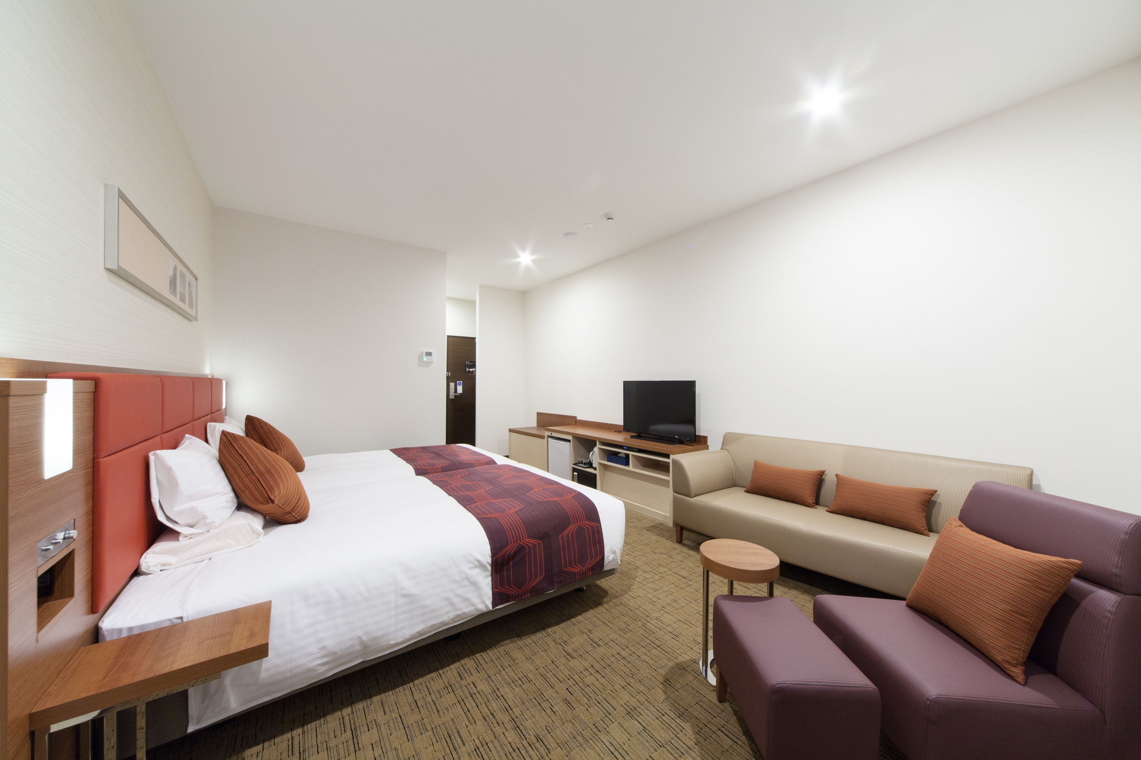 A hotel room with a bed, a sofa, a television, and a small table.