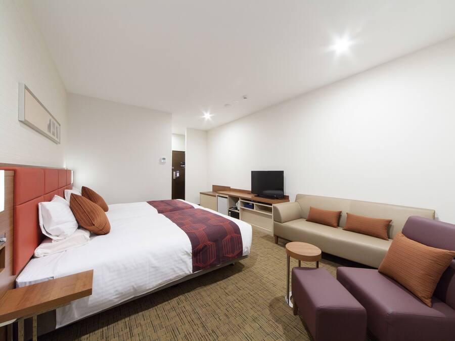 Una habitación de hotel con cama, sofá, televisor y una mesita.