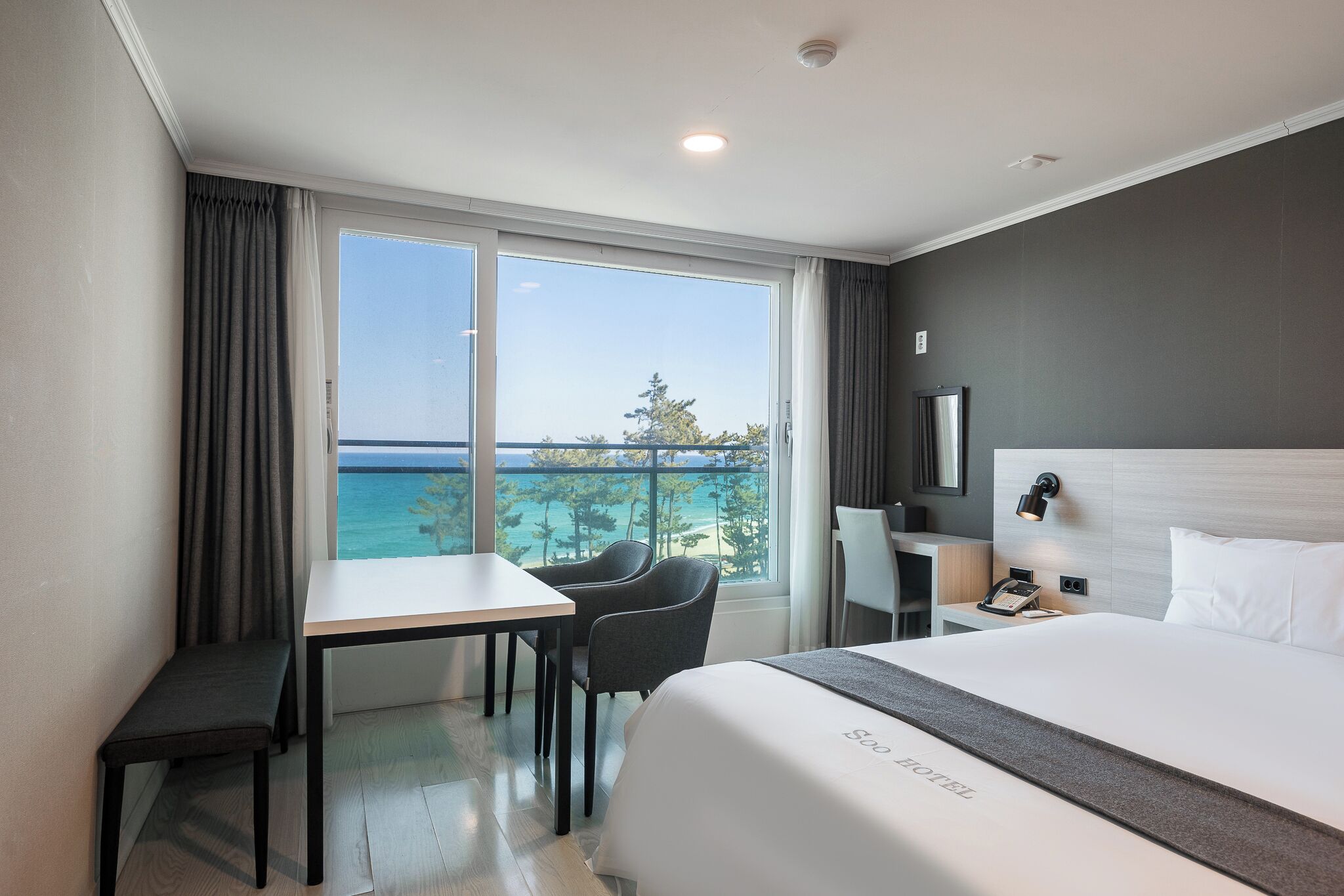 A hotel room with a large window, a bed, a desk, and a chair.