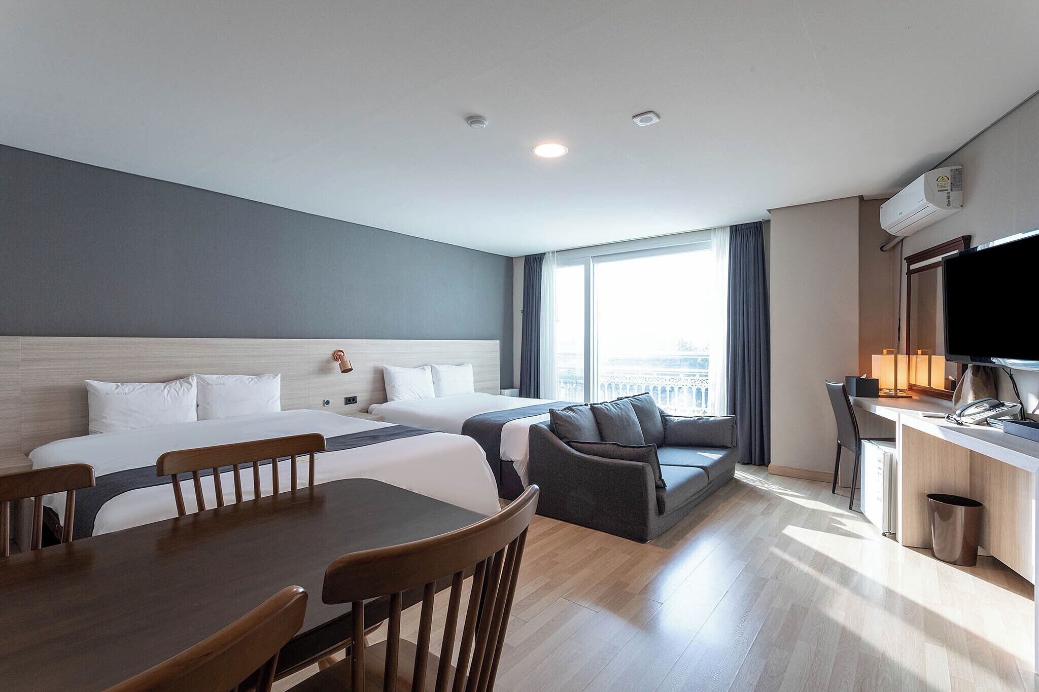 A hotel room with two beds, a dining table with chairs, a sofa, a desk with a computer, and a TV.