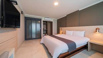 A modern hotel room with a large bed, a TV mounted on the wall, a wardrobe, and a bedside table with a lamp.