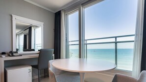 Une chambre d’hôtel équipée d’un bureau, d’une chaise et d’un petit réfrigérateur. Une grande fenêtre offre une vue sur la mer.