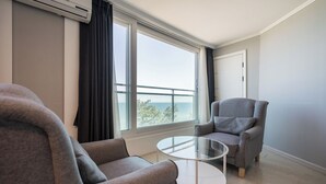 Un salon moderne avec deux fauteuils gris, une table basse en verre et une grande fenêtre donnant sur la mer.