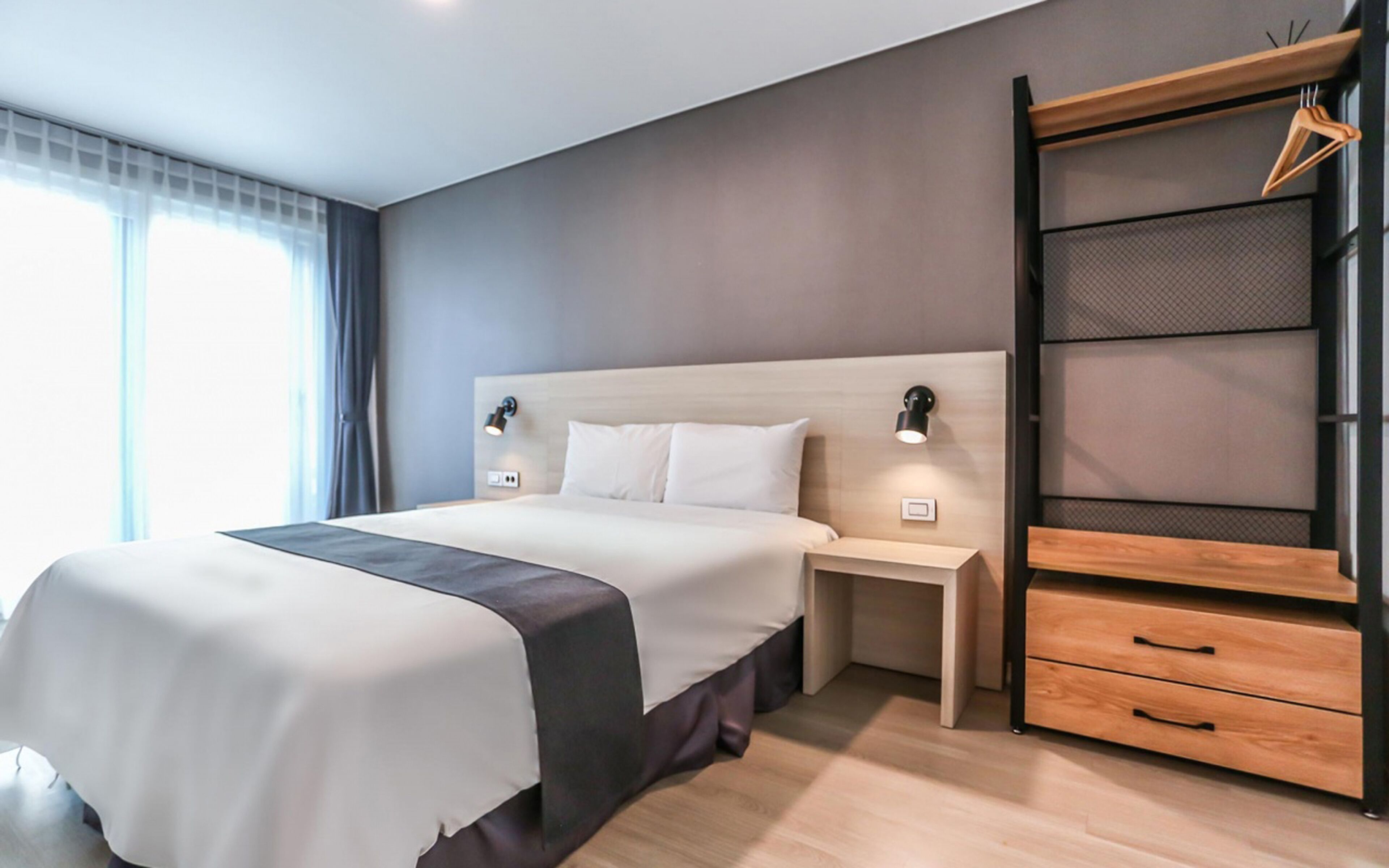 Une chambre d’hôtel moderne avec un grand lit, des tables de chevet, une armoire et une fenêtre avec des rideaux.