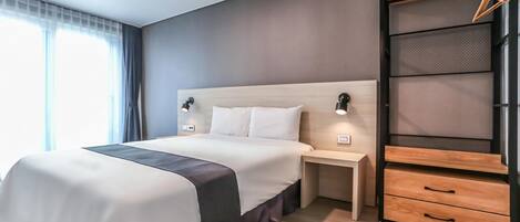 Une chambre d’hôtel moderne avec un grand lit, des tables de chevet, une armoire et une fenêtre avec des rideaux.