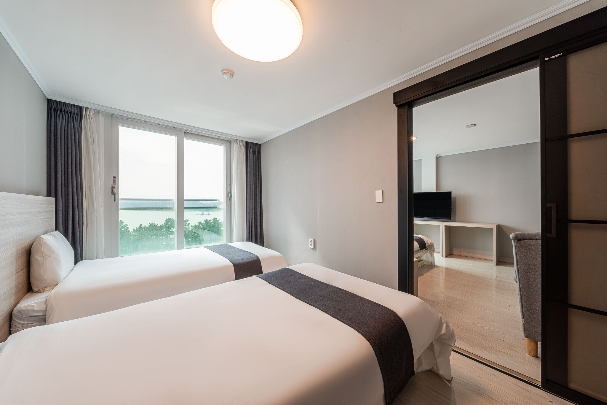 Habitación de hotel con dos camas, un ventanal con vistas, televisión y puerta corrediza que da a un balcón.