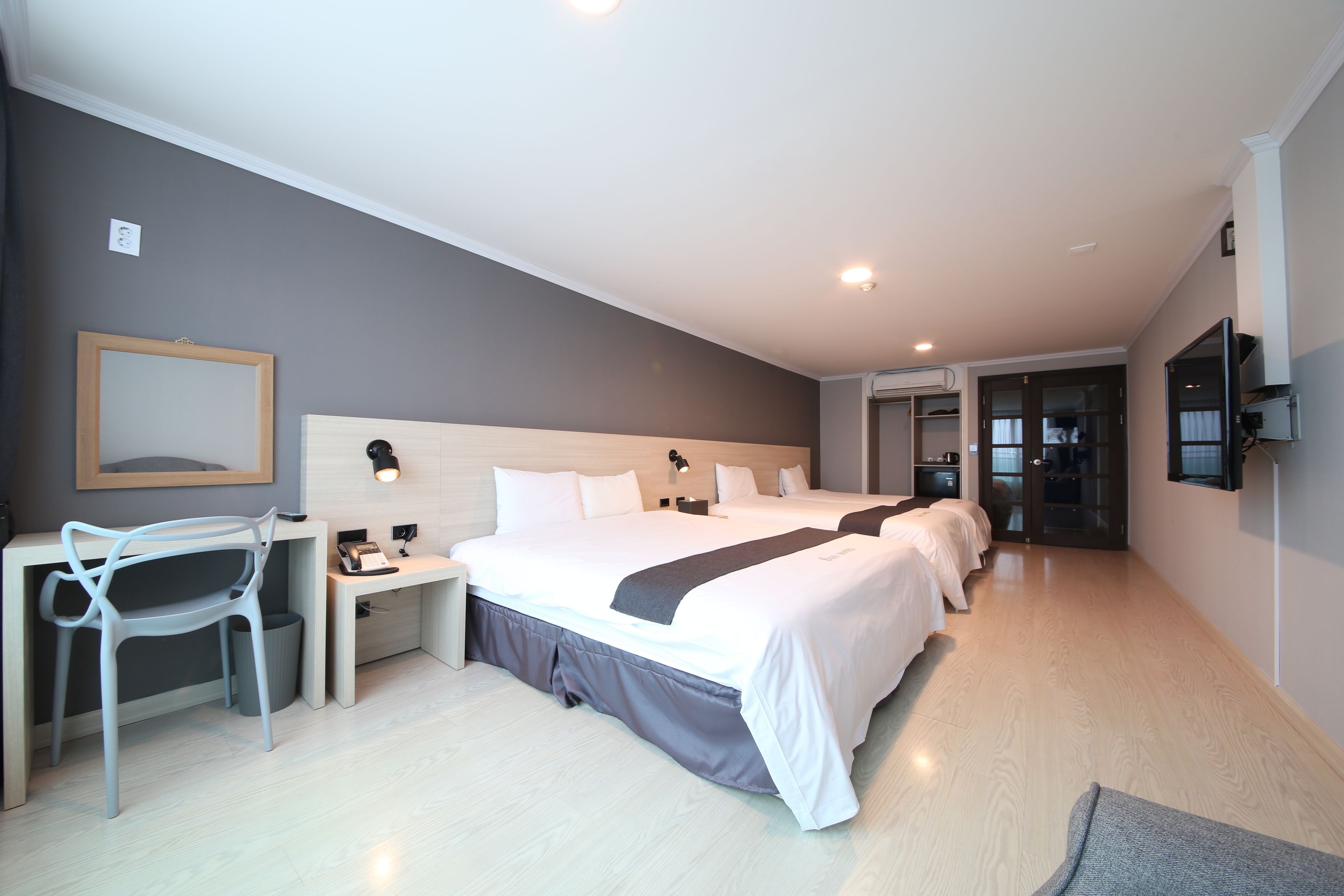 Una habitación de hotel moderna con una cama grande, un escritorio, una silla y un televisor montado en la pared.