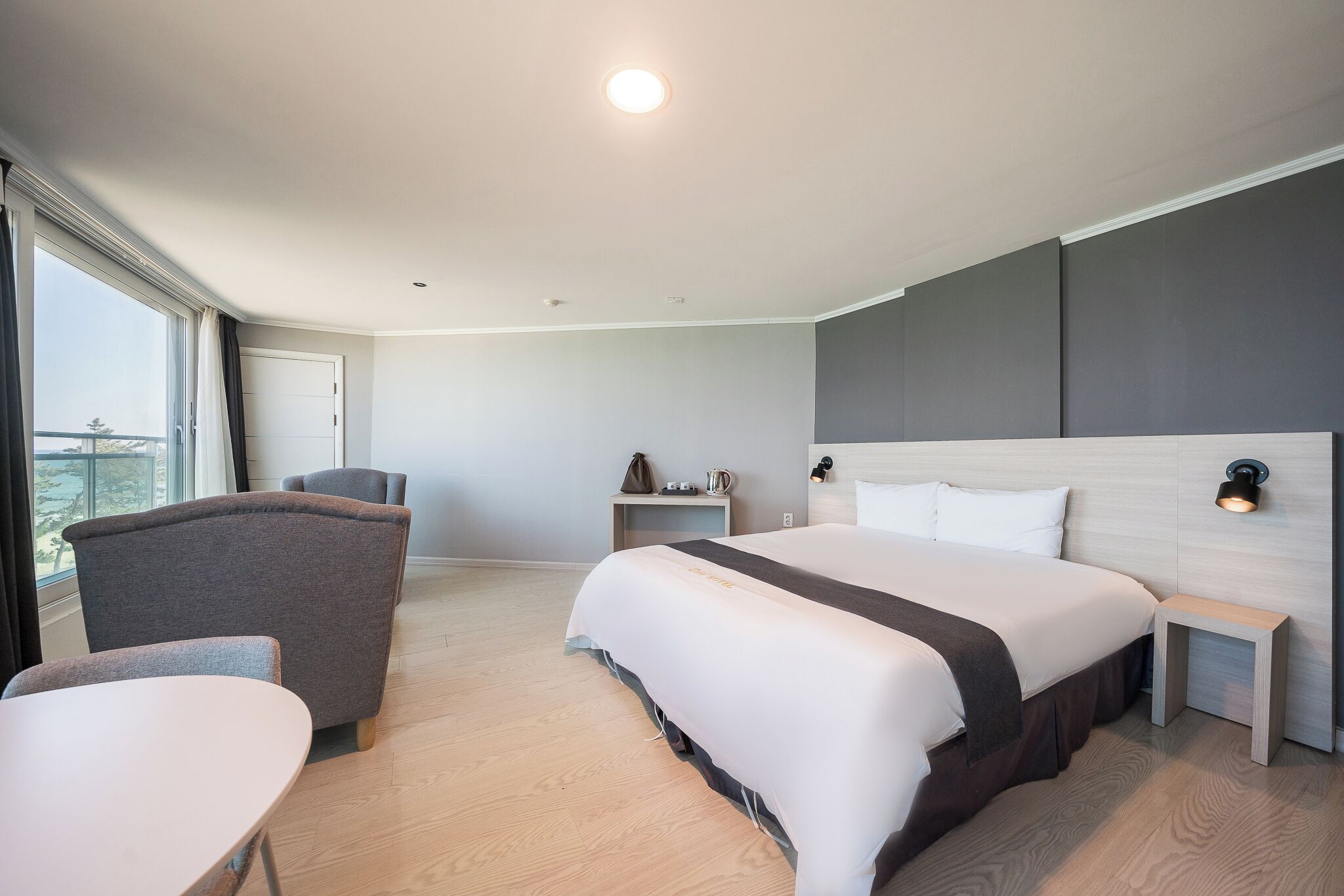 A modern hotel room with a large bed, a desk, a chair, and a view of the city.