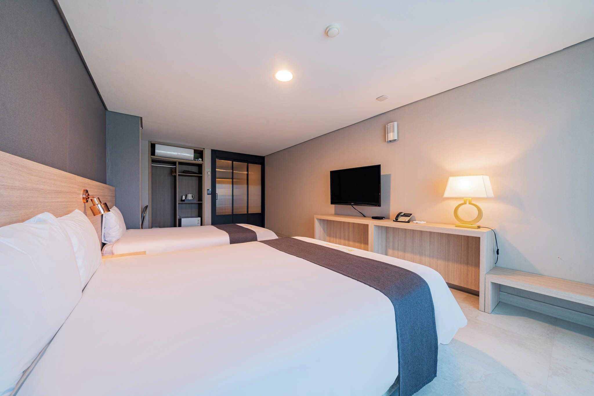 A hotel room with a large bed, a desk with a lamp, a television, and a wardrobe.