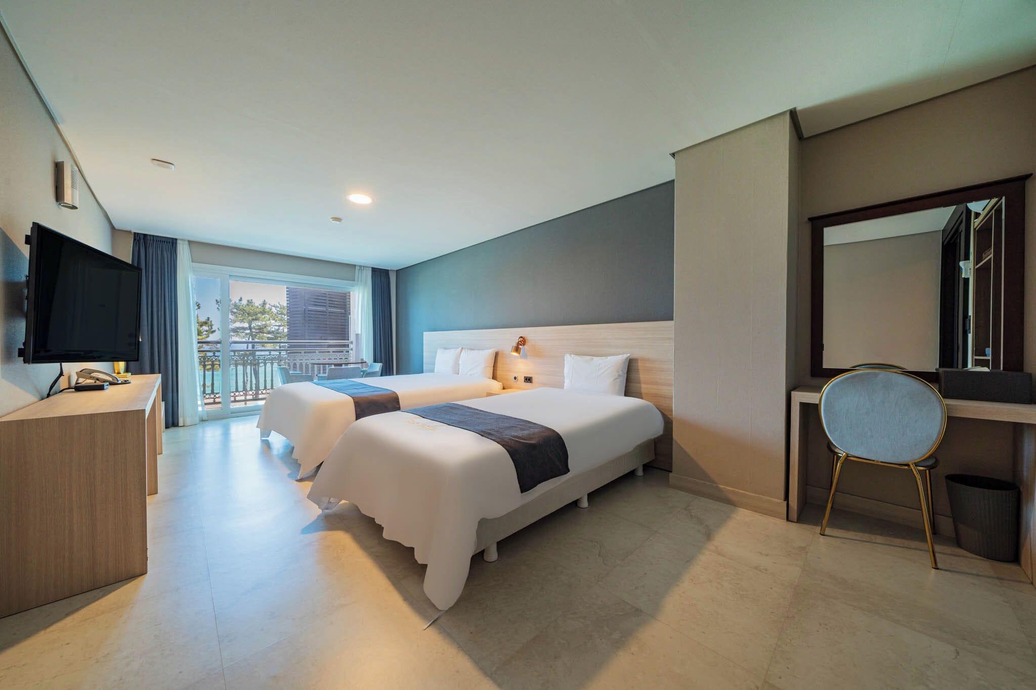 Habitación de hotel con dos camas, un escritorio, una silla, un televisor y un balcón con vistas.