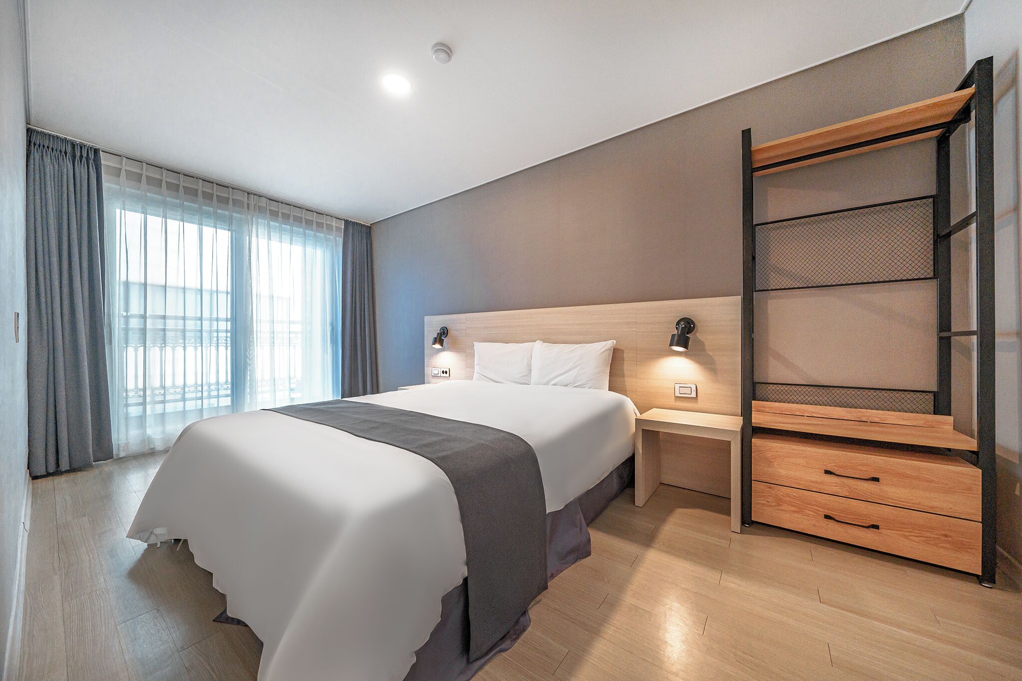 Una habitación de hotel moderna con una cama grande, una mesita de noche de madera y una estantería empotrada.