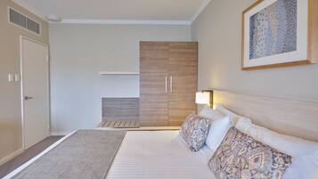Ein Schlafzimmer mit Bett, Kissen, Nachttisch, Kleiderschrank und einem Gemälde an der Wand.