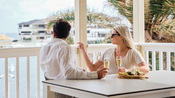 Una pareja cenando en una mesa al aire libre con vista al océano y palmeras.