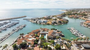Una marina con varias embarcaciones amarradas, rodeada de edificios residenciales y vista al mar.