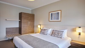 Una habitación de hotel moderna con una cama grande, un armario, lámparas de noche y una obra de arte enmarcada en la pared.