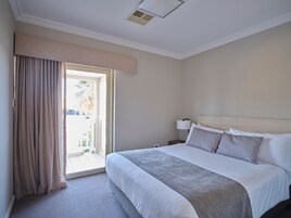 Una habitación de hotel con cama, mesita de noche, lámpara y vistas al exterior por una puerta corrediza.