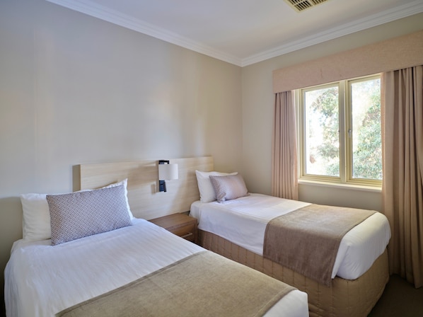 A hotel room with two beds, a nightstand with a lamp, a window with curtains, and a view of greenery outside. - The Marina Hotel - Mindarie (Mindarie)