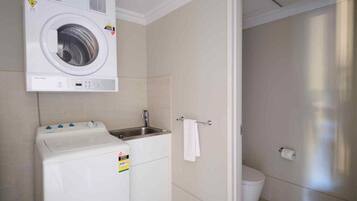 A compact laundry room with a washing machine, a small sink, and a toilet.