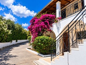 A building with a white exterior, a staircase with black railings, and a balcony with pink flowers. - Hotel Yannis Corfu (Corfu)