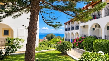 A coastal hotel with a view of the sea, featuring balconies, a garden, and a white building facade.