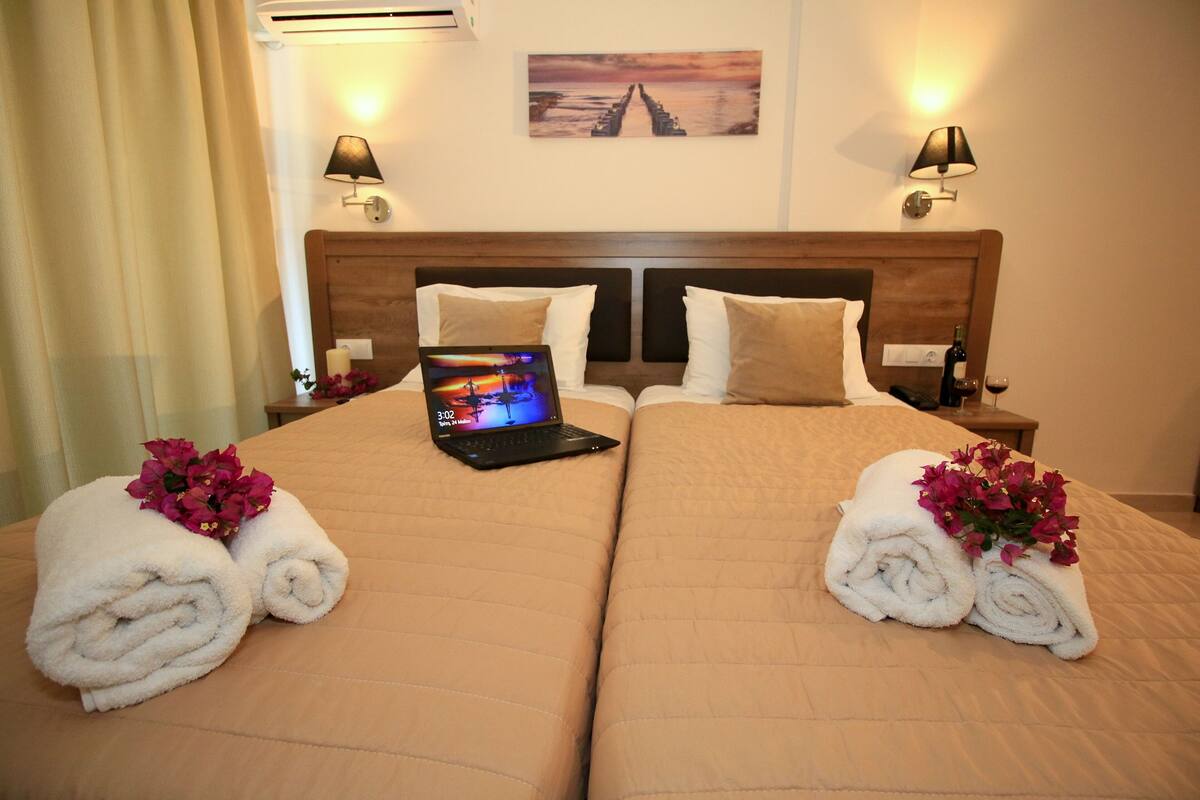 Una camera d'albergo con due letti, un portatile sul letto a sinistra e un quadro appeso al muro.