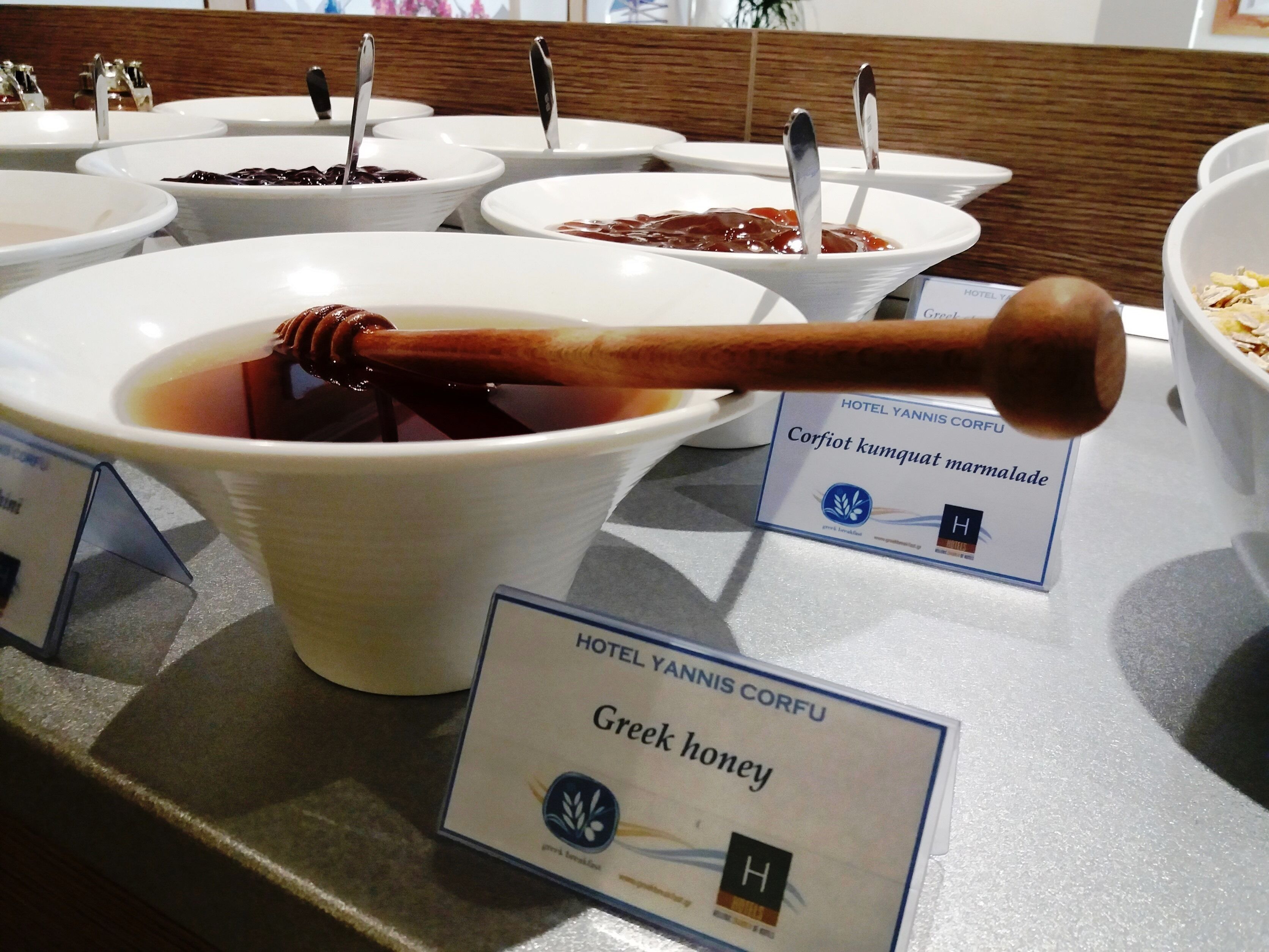 A buffet table with various food items, including a bowl labeled "Greek honey."