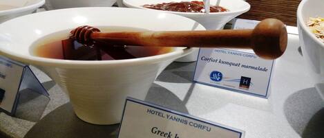 A buffet table with various food items, including a bowl labeled "Greek honey."