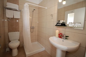 A bathroom with a toilet, shower, sink, and a shelf with toiletries. - Hotel Yannis Corfu (Corfu)