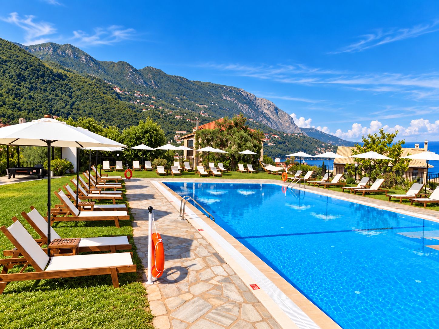 Una piscina con lettini e ombrelloni, immersa nel verde e con vista sulle montagne.