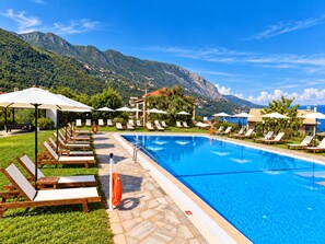 A swimming pool with lounge chairs and umbrellas, surrounded by greenery and mountains. - Hotel Yannis Corfu (Corfu)