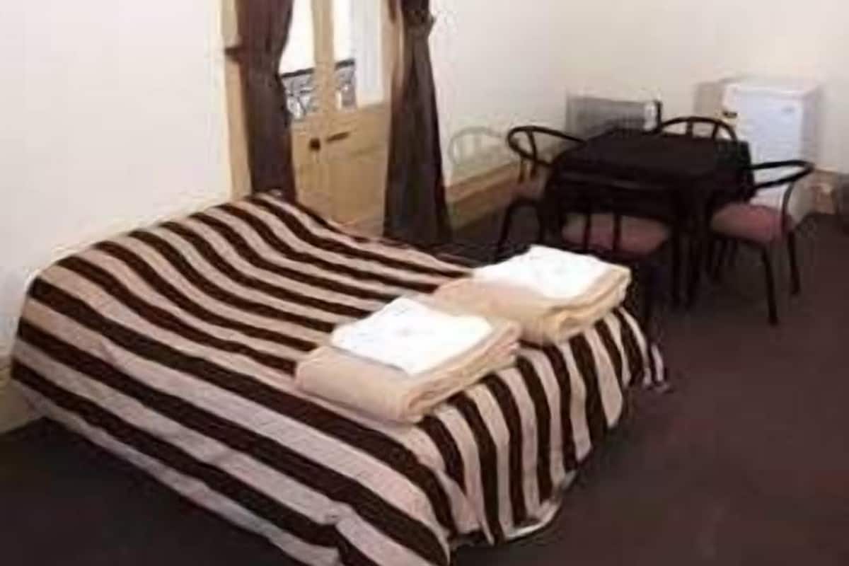 A single bed with striped bedding, a desk with a chair, and a small table with a chair.