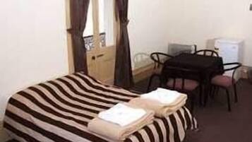 A single bed with striped bedding, a desk with a chair, and a small table with a chair.