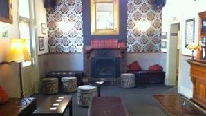 Ein gemütlicher Lounge-Bereich mit Kamin, ornamentalem Wandpapier und einer hölzernen Bank.