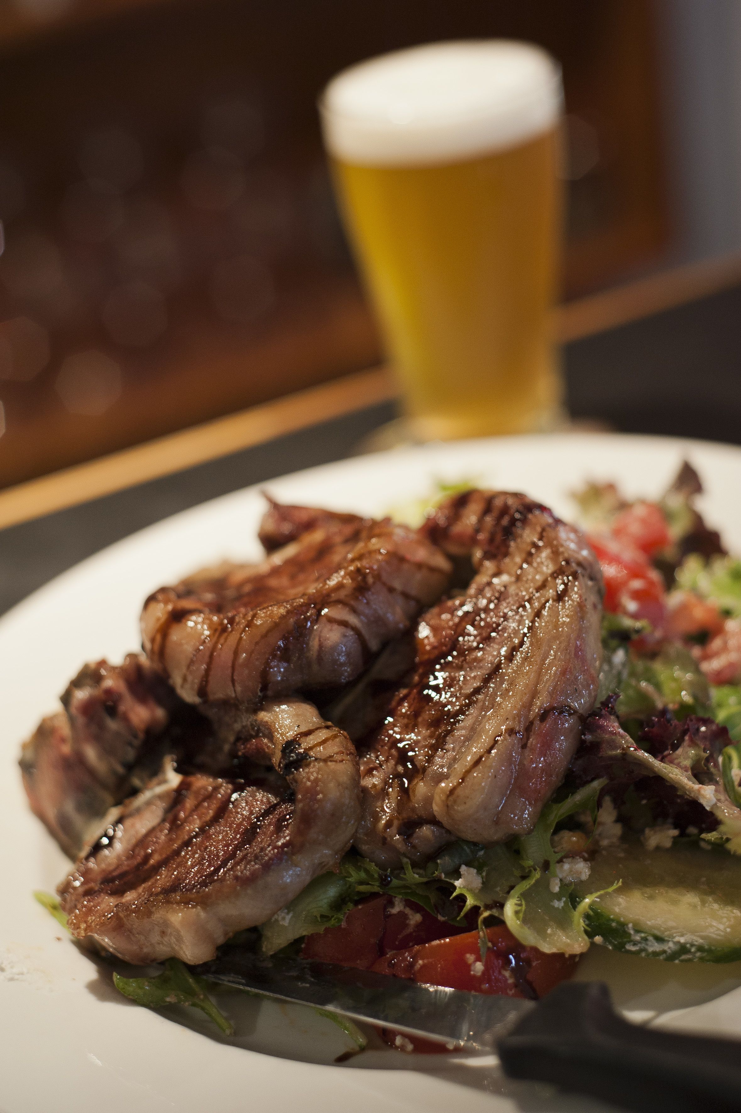 A plate of grilled meat with a side salad and a glass of beer.