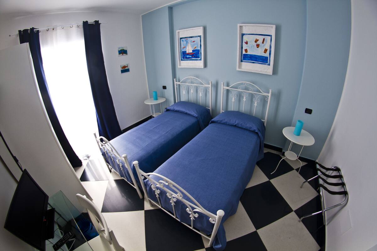 A room with two beds, a checkered floor, a small round table, and a wall with two framed pictures.