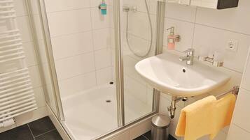 A modern bathroom with a glass-enclosed shower, a white sink, and a yellow towel hanging on a rack.