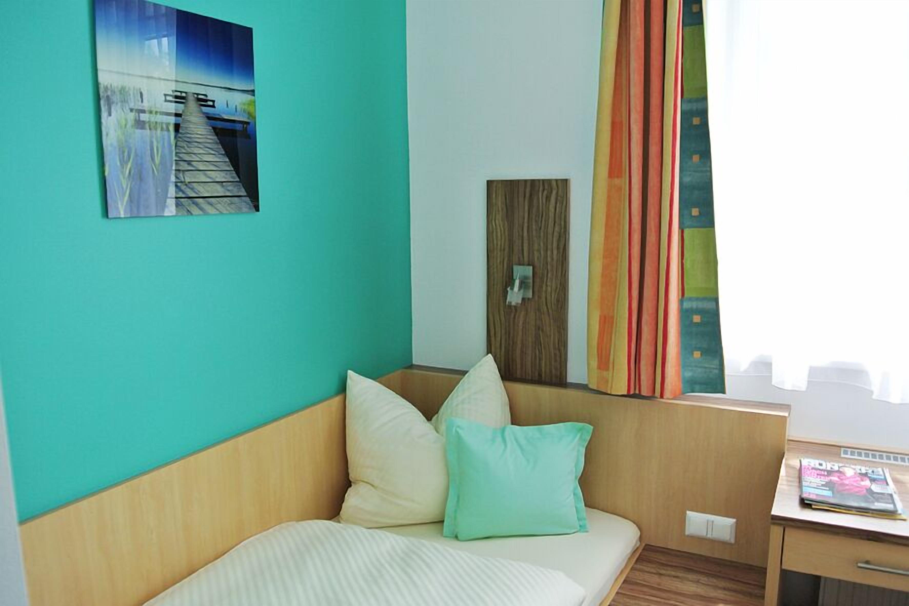 A hotel room with a bed, a wooden headboard, a painting of a bridge, and a window with curtains.