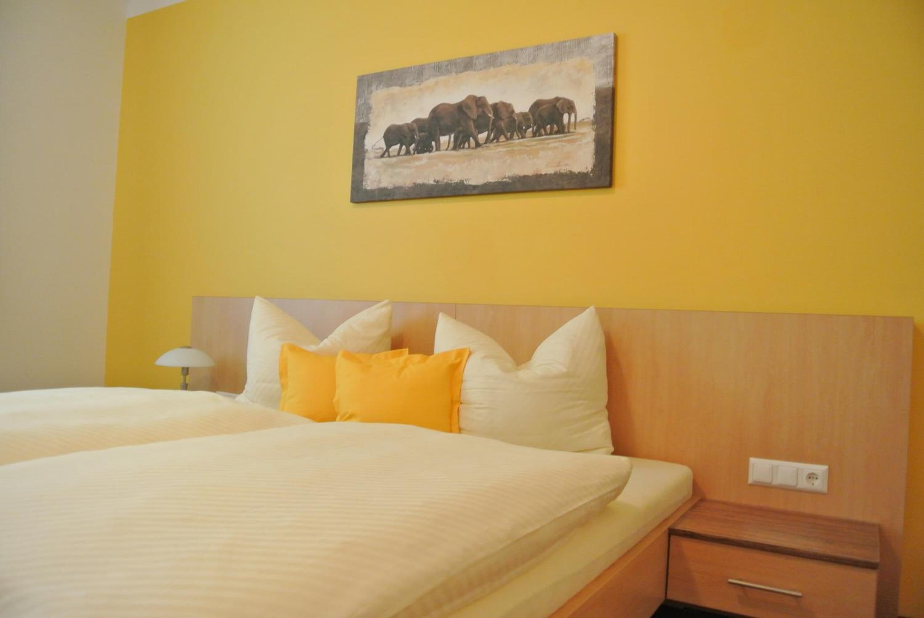Une chambre d’hôtel avec un grand lit, une table de chevet et un tableau représentant des éléphants, accroché au mur.